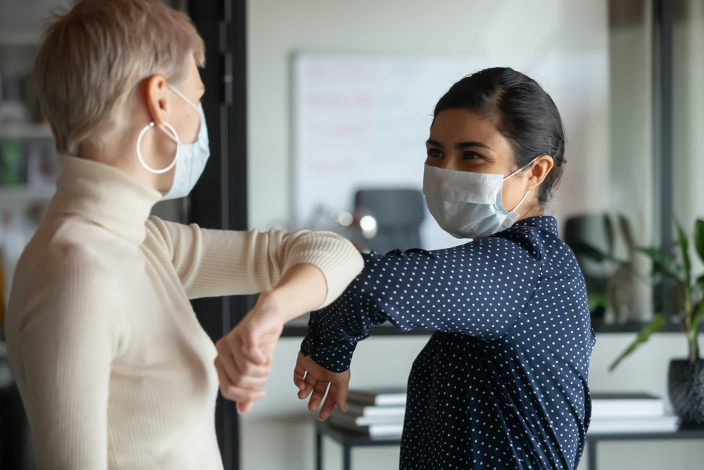 two women wearing masks elbow greeting